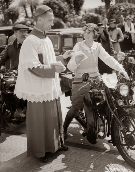 A reverend blesses the motorcycle of a woman who is learning to drive, 1938