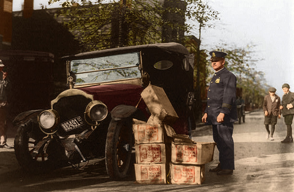 Policeman stands alongside a wrecked car and several cases of moonshine