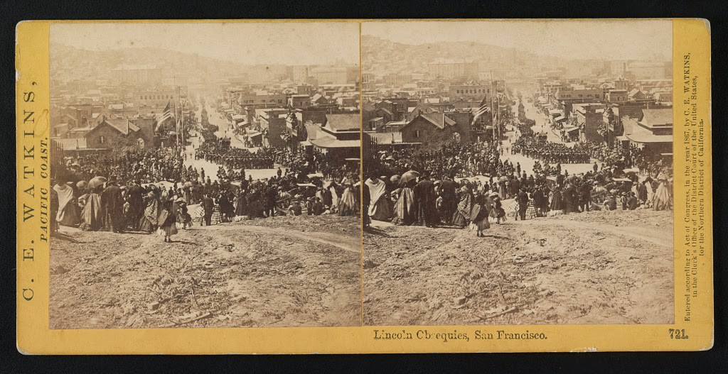 A view from a hill of a crowd observing a tribute to Abraham Lincoln on the street below, between 1865 and 1867.