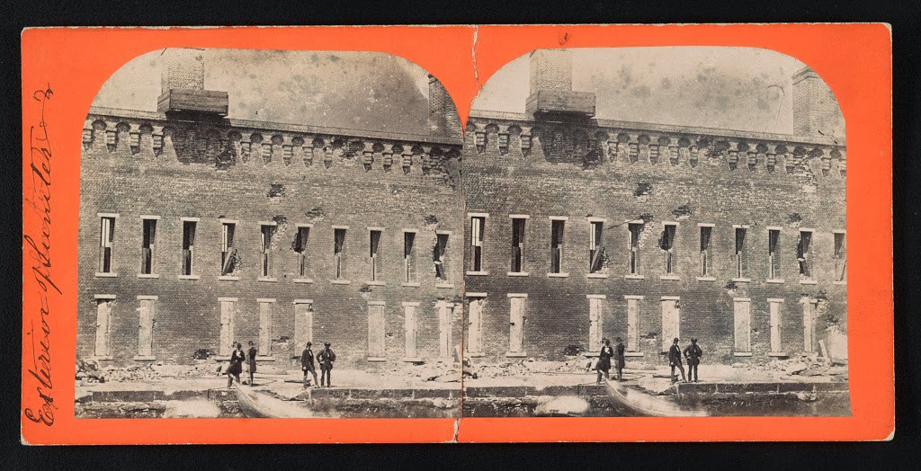 The exterior walls of Fort Sumter damaged by Confederate bombardment. Four men stand near a boat in the foreground, 1861.