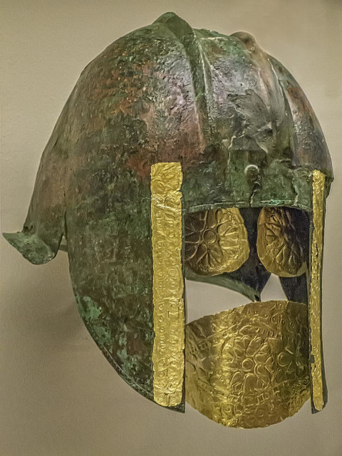 Funerary bronze helmet with gold eye and mouth pieces from the necropolis at Archontiko Greek 540-530 BCE. The deceased warrior was found lying on his back holding a gilded sword in his right hand, which bore a gold ring. A large embossed rosette, or the sun, decorates the center of its gold mouth and eyepieces.