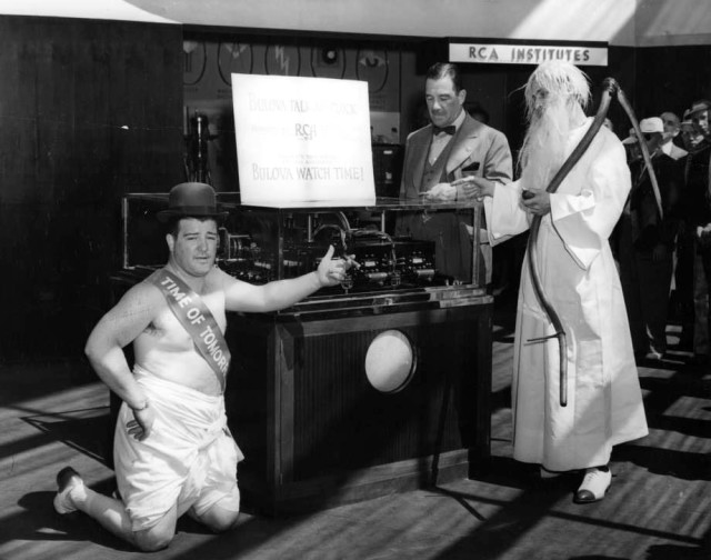 Bud Abbott, dressed as Father Time, and Lou Costello as Time of Tomorrow, look at the “Talking Clock.”