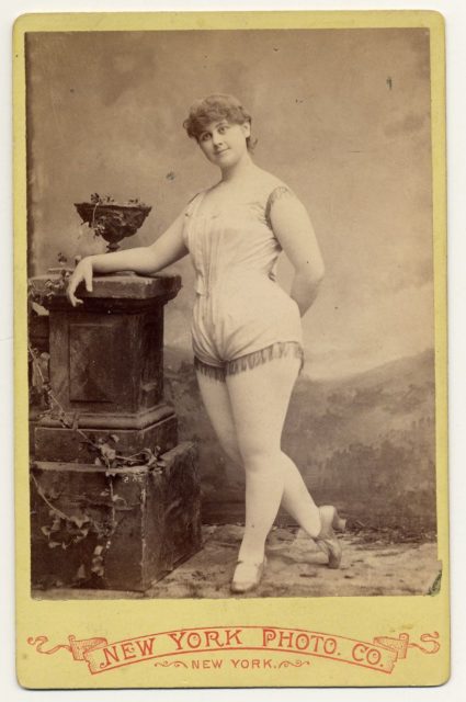 Clara Davenport in a short sleeveless costume fringed at legs and armholes.