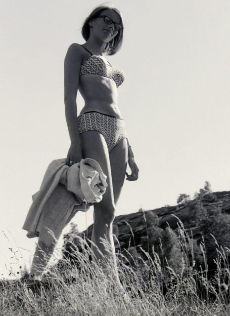 Girl in bikini standing high with sky background.Source