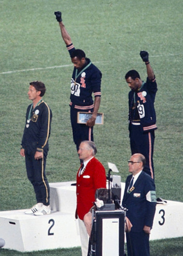 Gold medalist Tommie Smith (center) and bronze medalist John Carlos (right) showing the raised fist on the podium after the 200 m race. Source