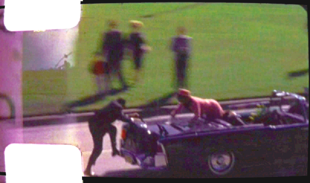 Kennedy reaching out across the back of the presidential limousine, as captured on the Zapruder film. Source: Wikipedia