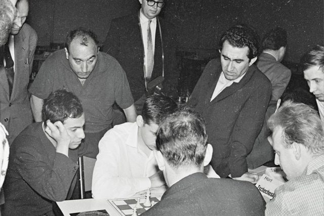 Petrosian (standing on right, with jacket) at the 1961 European Chess Team Championship. Seated, facing right, is Mikhail Tal, then world champion. Photo Credit