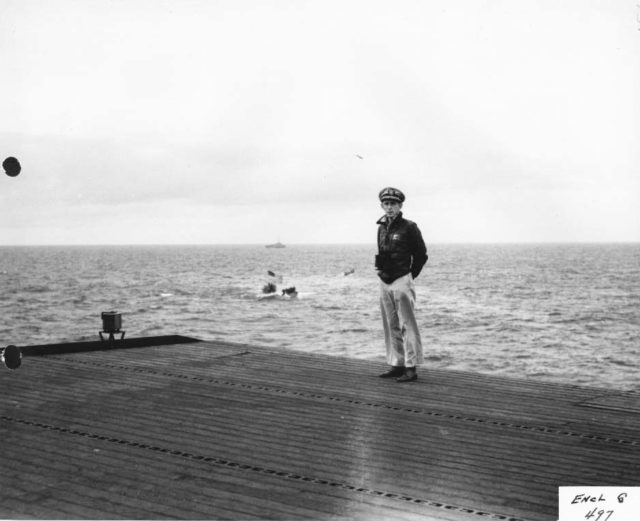 Captain Gallery on the flight deck with the captured sub in background.