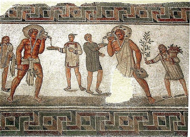 Roman mosaic from Dougga, Tunisia (2nd century CE): the two slaves carrying wine jars wear typical slave clothing and an amulet against the evil eye on a necklace; the slave boy to the left carries water and towels, and the one on the right a bough and a basket of flowers Photo Credit
