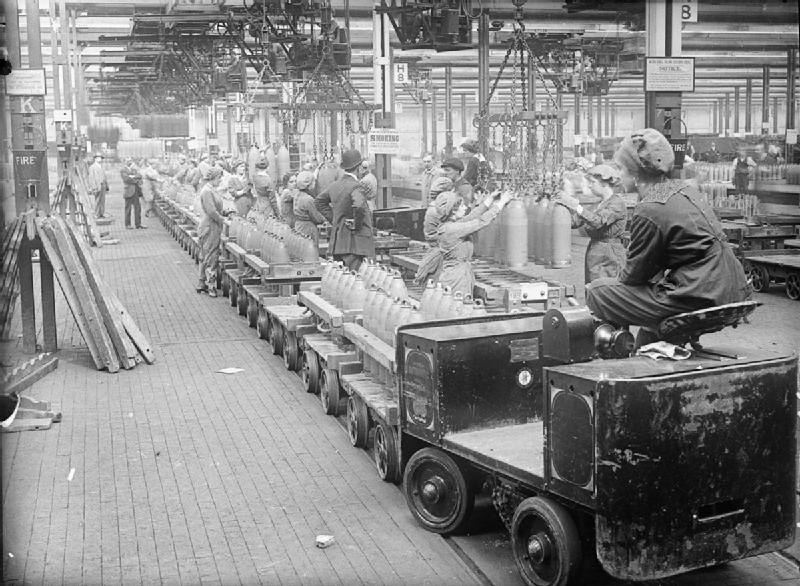 A woman drives a trolley train across a busy factory floor at the National Filling Factory, Chilwell