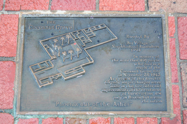 A memorial plaque embedded in the sidewalk near the site of the fire. It reads: “The Cocoanut Grove.Photo Credit