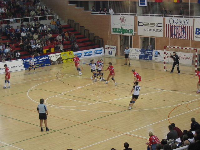 Women’s handball: Players moves towards the goal prior to throwing the ball; the goalkeeper defends the goal. photo credit
