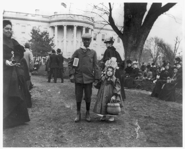 Two children hold hands on the front lawn of the White House during the 1898 Easter Egg Roll