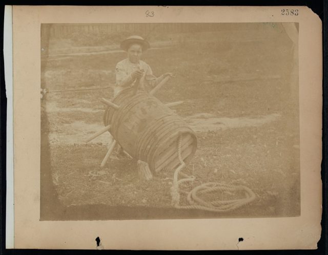 A child leaning against a barrel with wooden spikes. Photo Credit