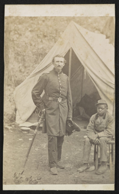 Major Luzerne Todd of Co. D, 23rd New York Infantry Regiment and Co. B, 86th New York Infantry Regiment in uniform with sword and unidentified young African American servant in front of a tent. Photo Credit