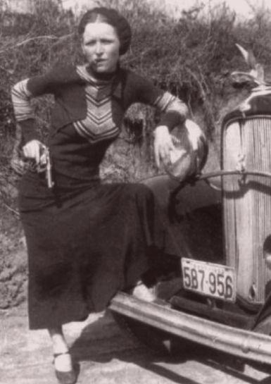 Notorious criminal Bonnie Parker smoking a cigar and standing in front of a Ford Model V-8