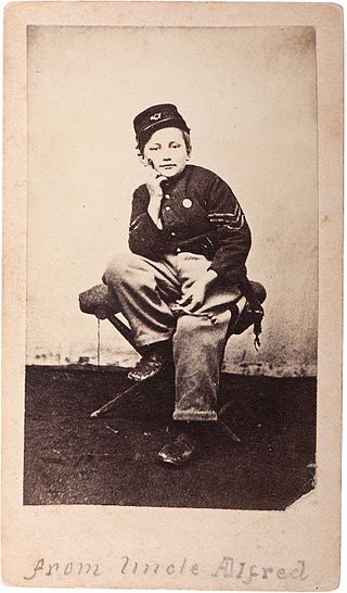 Carte providing a full-length portrait of Johnny Clem dressed in uniform, seated on a campstool, verso with Hall, Lawrence (MA) imprint and printed biographical sketch.