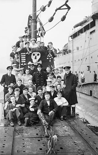 The crew of Thunderbolt and their ‘Jolly Roger’ flag, after a patrol in the Mediterranean.