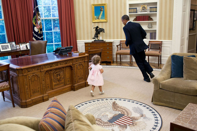 President Barack Obama runs around the Resolute desk in the Oval Office.