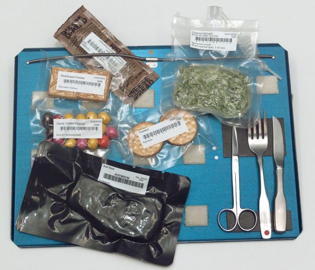 Food aboard the Space Shuttle served on a tray. Note the use of magnets, springs, and Velcro to hold the cutlery and food packets to the tray