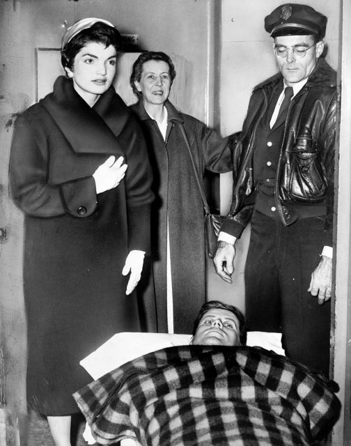 Kennedy lying on a gurney following spinal surgery, accompanied by Jackie, December 1954