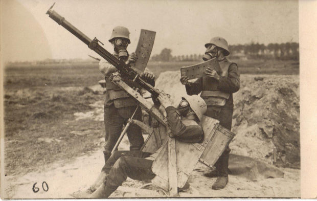 Three German soldiers in body armor and gas masks demonstrate operating a 2cm Becker-Flugzeugkanone.
