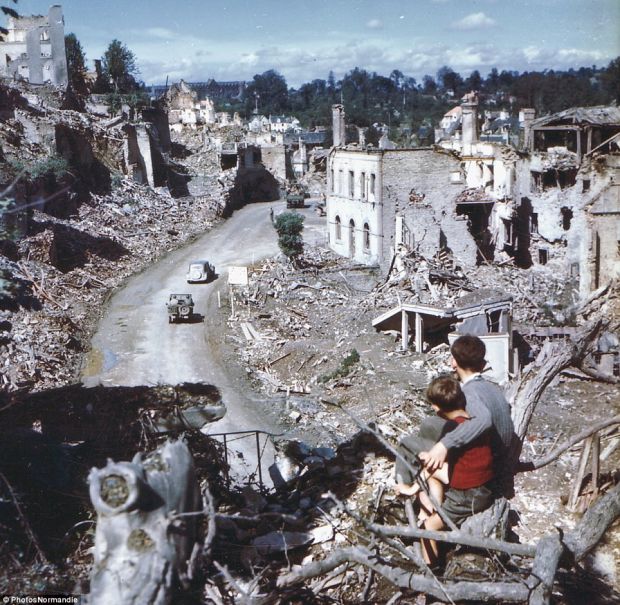 Two boys look onto the aftermath of the D-Day invasion as American soldiers drive through the town of St. Lo. France, 1944.