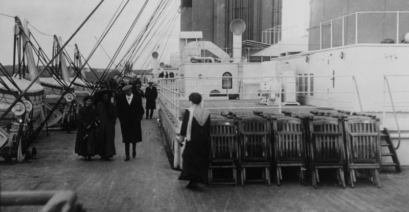 Passengers stroll passed chairs on the deck of the Titanic (1912).