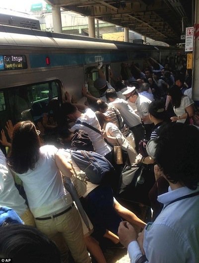A crowd pushes against a train to rescue a stranger caught in the gap between the train and the platform.
