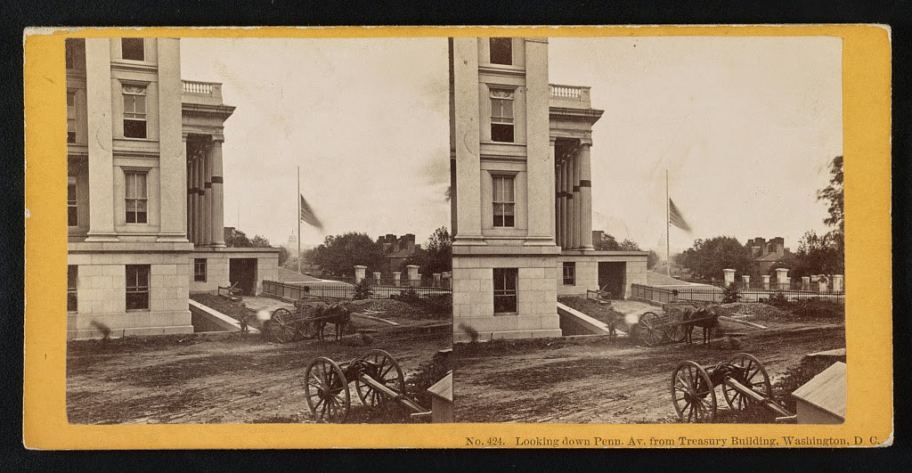 A view of Pennsylvania Avenue in Washington D.C. after the death of Abraham Lincoln showing mourning bands draped on columns, and a flag at half staff. A caisson is parked in the foreground, 1865.