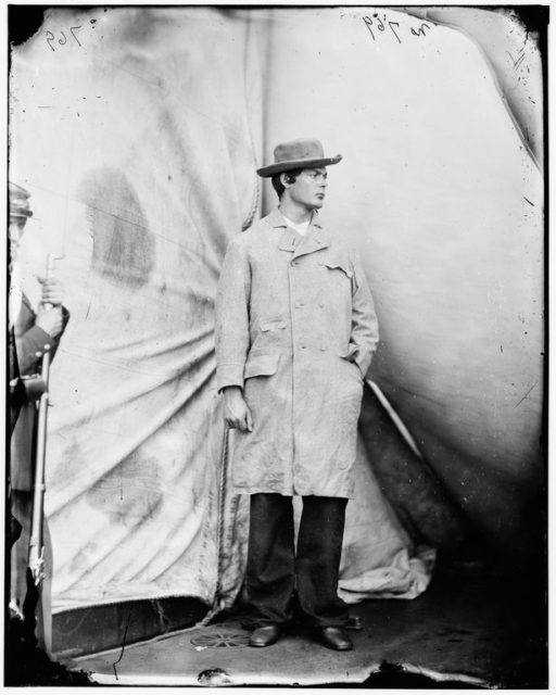 Lewis Powell poses in a coat and hat while under guard.