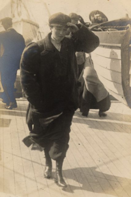 The woman of the couple on the ferry, wearing a masculine-looking coat and hat.