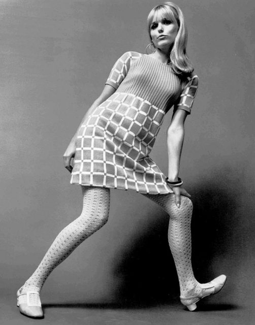 Photo of a model wearing a sweater-knit dress with patterned tights and chunky shoes.Source