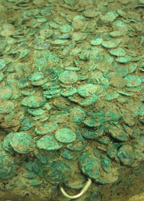 The excavated hoard undergoing cleaning and investigation. Jewellery can be seen protruding from the mass of coins. - Source
