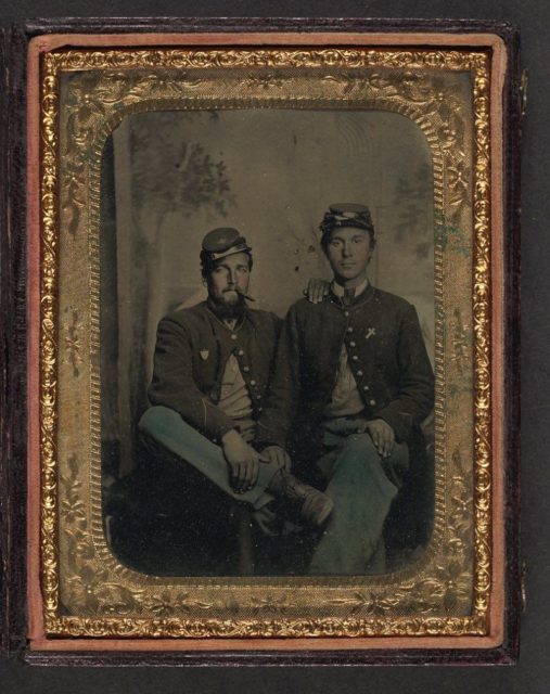 Two unidentified soldiers in Union uniforms in front of painted backdrop showing trees