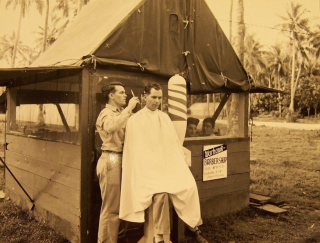 Looking for a trim on a South Pacific island, look for the Warhawk Barber Shop with its barber pole made of a bomb shell. (NARA)