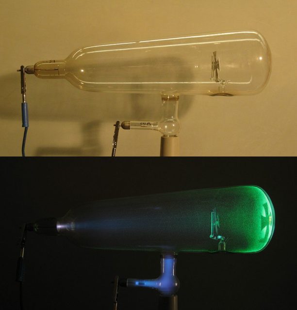 A Crookes tube: light and dark. Electrons (cathode rays) travel in straight lines from the cathode (left), as shown by the shadow cast by the metal Maltese cross on the fluorescence of the righthand glass wall of the tube. The anode is the electrode at the bottom. Photo credit