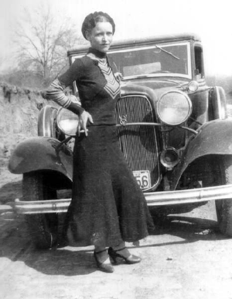 Bonnie Parker from Bonnie and Clyde standing in front of a Ford Model 18 (aka Ford V-8).
