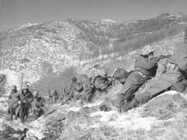 Marines under the cover of a large boulder engaging the Chinese.