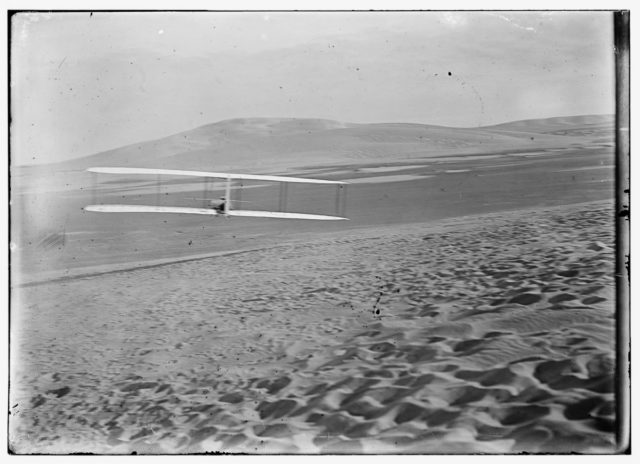 Orville making right turn, showing warping of wings, hill visible in front of him Photo Credit 