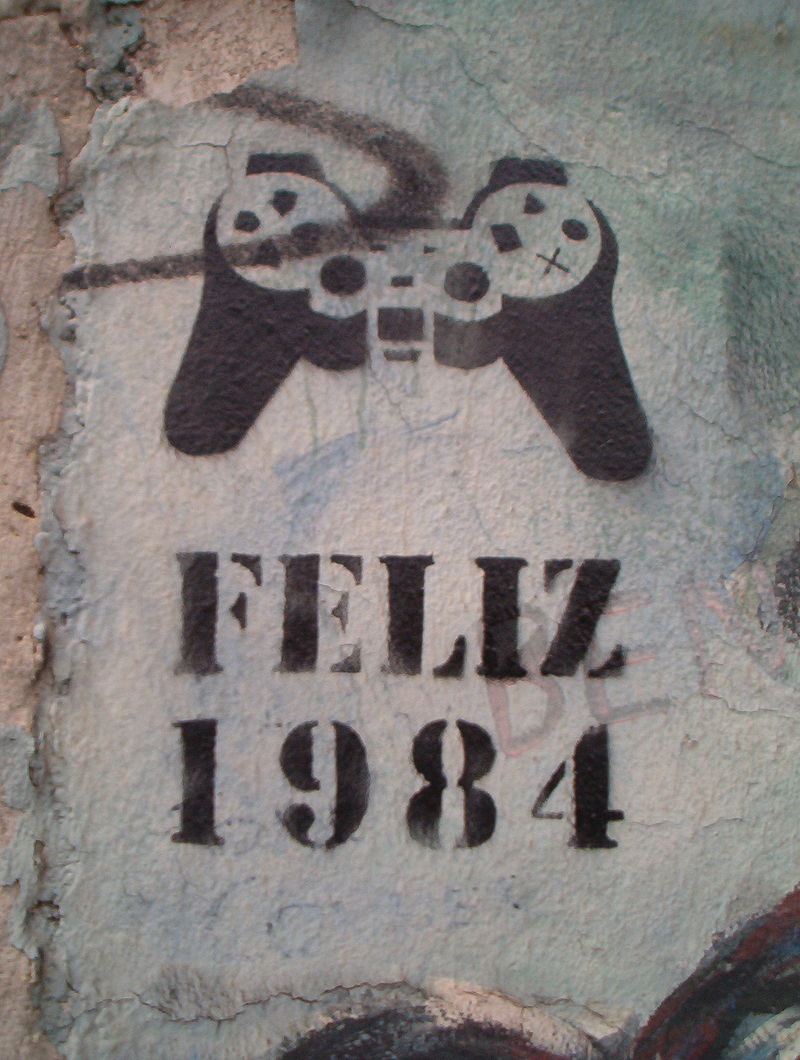 “Happy 1984” stencil graffiti, denoting mind control via a video game controller, on a standing piece of the Berlin Wall, 2005.