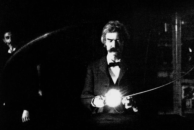 Mark Twain in the lab of Nikola Tesla, spring of 1894. Twain is holding Tesla’s experimental vacuum lamp, which is powered by a loop of wire which is receiving electromagnetic energy from a Tesla coil (not visible). Tesla’s face is visible in the background.