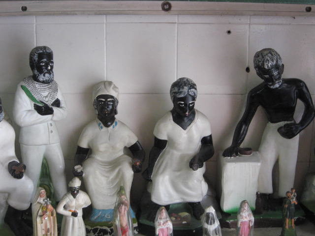 Small Umbandan statues of pretos velhos or “old slaves”, spirits of those who died enslaved. The statues represent suffering, compassion, forgiveness, and hope. The Umbanda religion recognizes Anastacia as a saint and martyr. Photo Credit