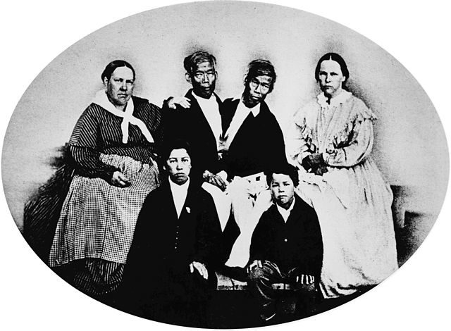 Photograph of the Bunker family taken in1865 by Mathew Brady. On the right is Chang, his wife Adelaide, and their son Patrick Henry; on the left is Eng, his wife Sarah, and their son Albert