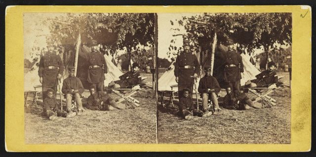 Stereograph showing Capt. B.S. Brown (left); Lt. John P. Shaw, Co. F 2nd Regt. Rhode Island Volunteer Infantry (center); and Lt. Fry (right) with African American men and boy at Camp Brightwood, D.C.. Photo Credit