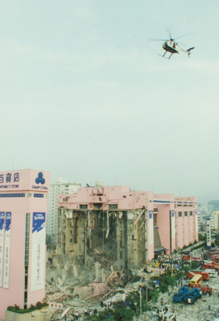 View of the Sampoong building shortly after the collapse. With the exception of the end tower, the entire south wing fell upon itself. A rescue helicopter is seen flying above, photo credit