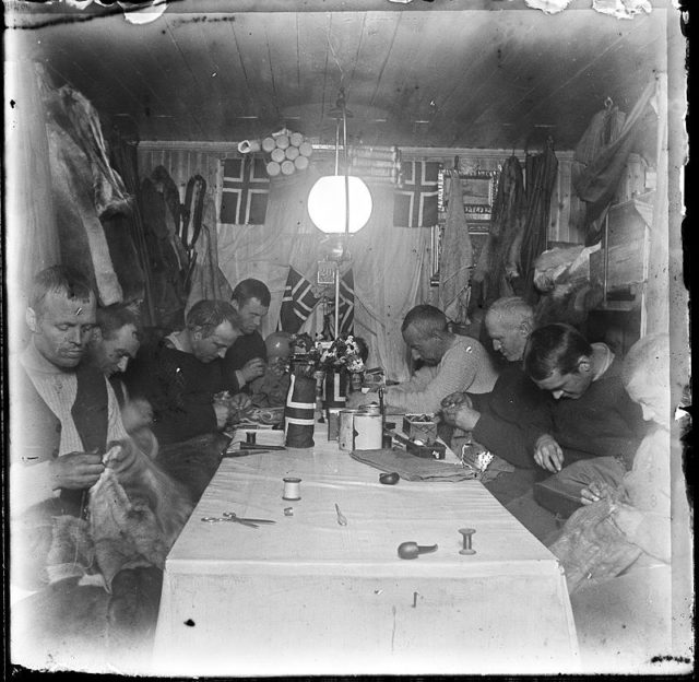 Amundsen and his team engaged in fitting clothes at Framheim, polar winter 1911.