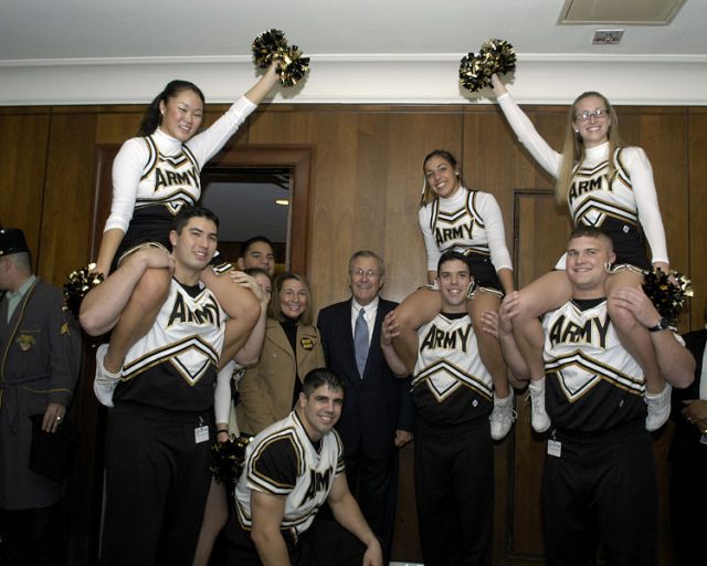 Secretary of Defense Donald H. Rumsfeld (center) is greeted outside his Pentagon office by the West Point Academy cheerleaders and band on Dec. 3. 2004. The cadets are promoting esprit de corps in the Pentagon for the upcoming Army/ Navy football game on Dec 4, 2004.