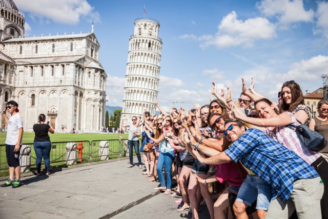 Pisa, Italy – June 22, 2015: Large group of tourists posing and having fun doing funny portraits in front of the Leaning Tower of Pisa during a beautiful summer day.
