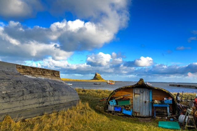 Holy Island of Lindisfarne, United Kingdom – February 1, 2015: Lindisfarne Castle is in the background behind former fishing boats now used as storage sheds by the fishermen on Holy Island, Northumberland.